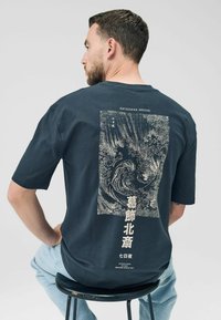 Short-sleeve navy blue cotton t-shirt featuring a white print of Hokusai's artwork and text on the back, relaxed fit, and crew neckline.
