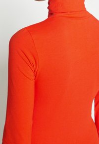 Röd polotröja i stretchigt material. Åtsittande design med långa ärmar, med hög halsringning och en slät yta.