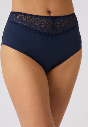 Sous-vêtement taille haute bleu marine avec bordure en dentelle et petit nœud porté sur la partie inférieure du torse et le haut des cuisses d’une personne.