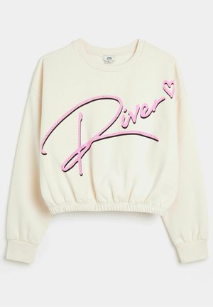 Kremowa krótka bluza z długimi rękawami, elastycznym dołem oraz dużym różowym napisem „River” z serduszkiem z przodu.