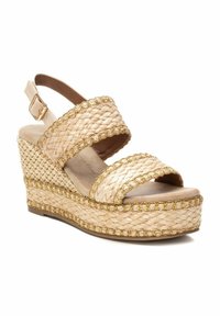 Sandalo con zeppa in paglia intrecciata di colore beige chiaro, con accenti dorati metallici sulle cinghie, design open toe e suola piattaformata texturizzata.