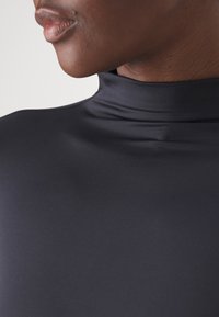 Haut noir à col montant avec une texture lisse et extensible, de coupe ajustée, présentant un gros plan sur l'encolure et la partie supérieure de la poitrine.