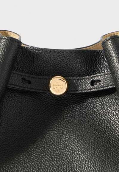 Črna usnjena torba z teksturo, s poševnimi ročaji in osrednjim zlatim krožnim logotipom na zaponki.