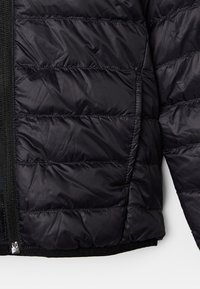 Chaqueta negra tipo acolchada con secciones acolchadas, cierre de cremallera y puños elásticos. Tela lisa y brillante con una textura ligera.