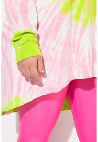 Camisa de gran tamaño en tie-dye rosa y verde con mangas largas, que presenta un dobladillo curvado, combinada con leggings rosa brillante.