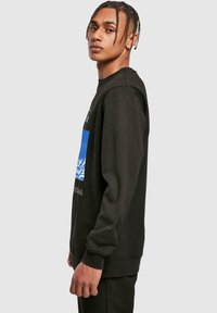 Svart sweatshirt med lange ermer, med en blå grafisk design på framsiden og hvit tekst. Glatt tekstur, avslappet passform.