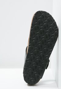 Svart flip-flop stil sandal med en texturerad gummisula och en korkinläggssula, med ett böjt mönster på undersidan.