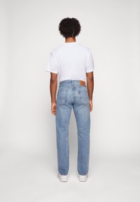 Faded blue denim jeans with a straight-leg fit, featuring a brown leather patch at the back, five pockets, and subtle stitching details.