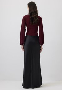 Burgundska dolgimi rokavi bluza z nabranimi rokavi v kombinaciji z elegantno, črno, dolgo satenasto krilo. Gladka tekstura z oprijetim silhueto.