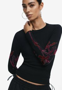 Maglione nero a maglia con maniche lunghe e motivi floreali ricamati in tonalità di rosso e viola. Polsini e vita a costine.