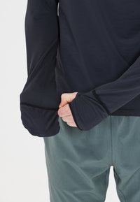 Langärmliges, dunkelblaues Hemd aus leichtem Stoff, mit Daumenlöchern an den Manschetten und flachen Nähten für Komfort, kombiniert mit grünen Hosen.