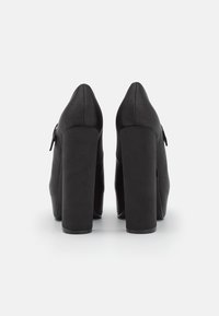 Czarne szpilki o gładkiej fakturze, zwężającym się nosku i masywnym obcasie. Posiadają ozdobę w postaci kokardy po boku.