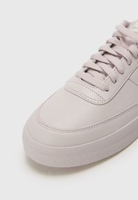 Adidași violet deschis cu un superior din piele netedă, vârf rotund și talpă din cauciuc texturat. Dispune de șireturi plate și detalii discrete de cusătură.