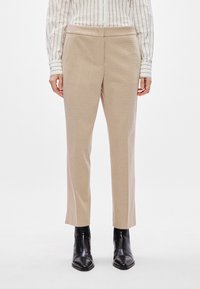 Calças bege ajustadas com um padrão texturizado, corte reto e cintura média, combinadas com botas pretas até ao tornozelo.