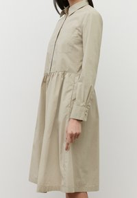 Abito camicia beige realizzato in tessuto leggero, con collo a camicia, maniche lunghe, chiusura con bottoni e cucitura in vita arricciata.