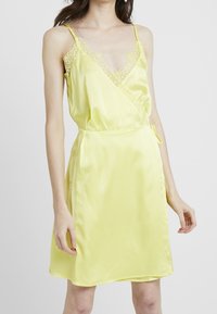 Keltainen satiinimekko, jossa on V-pääntie, pitsireunus hartioilla ja kietaisusuunnittelu. Ominaisuuksiin kuuluu sivusite ja sileä, kiiltävä pinta.