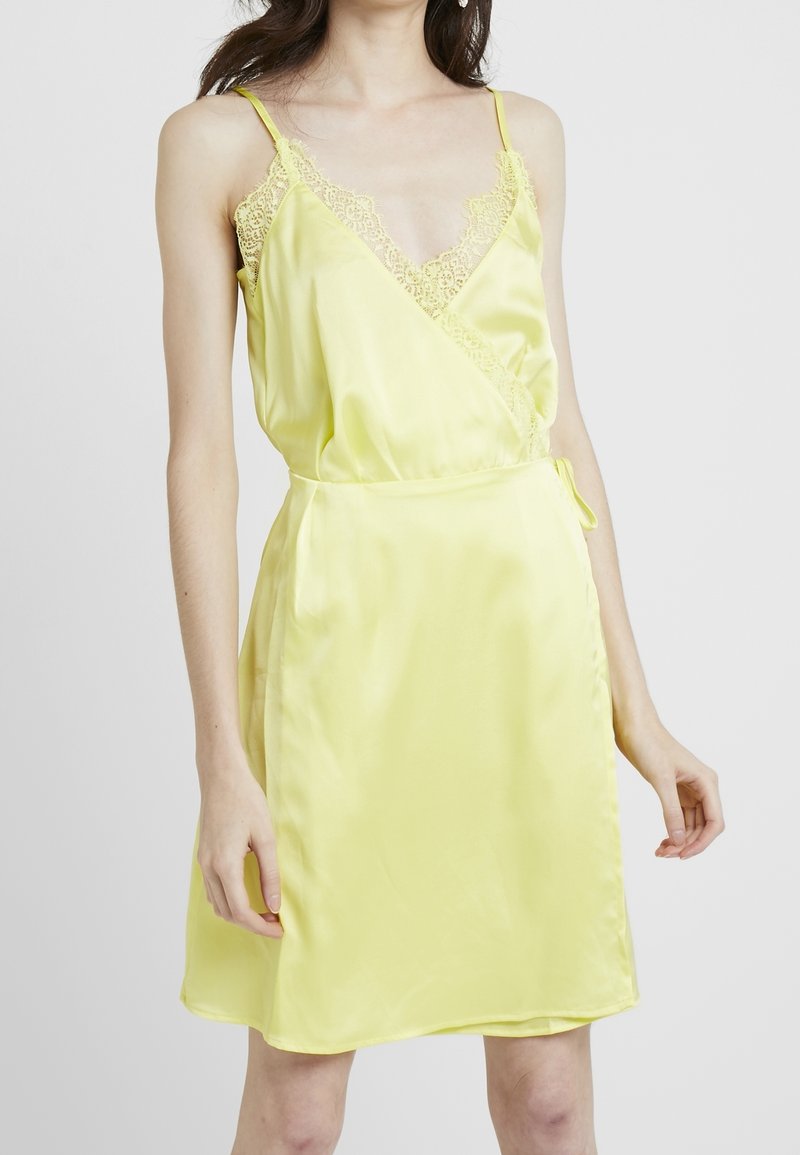 Keltainen satiinimekko, jossa on V-pääntie, pitsireunus hartioilla ja kietaisusuunnittelu. Ominaisuuksiin kuuluu sivusite ja sileä, kiiltävä pinta.