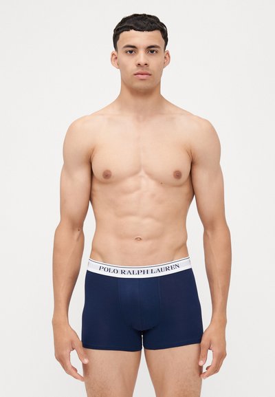 Mornarski bokserice z belim pasom, na katerem je napis "POLO RALPH LAUREN". Gladek material, prilegajoča zasnova in dolžina do sredine stegen.