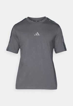 T-shirt de sport gris en tissu doux, avec des manches courtes, un col rond et un petit logo réfléchissant sur la poitrine. Accents transparents sur les épaules.
