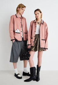 Dva modelky majú na sebe koordinované outfity. Rúžová košeľa s čiernym lemom, šedé šortky a sukňa s leopardím vzorom. Čierne topánky a akcenty dotvárajú vzhľad.