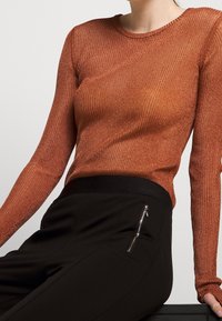 Maglietta a maniche lunghe di color ruggine con righe, abbinata a pantaloni neri con tasca con zip, tessuto morbido e design aderente.