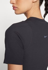 Mustmust värvi ribatatud lühikeste varrukatega T-särk ümmarguse kaelusega. Tagaküljel on peen Nike logo heledas hallis, mis rõhutab vormistatud disaini.
