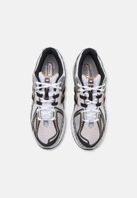 Paire de chaussures de running New Balance 1906R blanches et noires avec tissu mesh et lacets, vues de dessus sur fond gris.