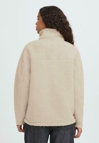 Bee�ži värvusega fliisjope kõrge kraega ja tekstureeritud välispinnaga. Omadusteks on langevad õlad ja lõõgastunud lõige. Seljal õmbluste detailid.