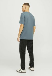 Korte mouwen, blauwe t-shirt gecombineerd met zwarte broeken en witte sneakers, gezien vanaf de achterkant. Gladde textuur met een ontspannen pasvorm.