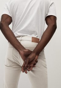 Camiseta blanca combinada con jeans beige claro. Los jeans presentan un detalle de cuero en la cintura y los bolsillos traseros, con un diseño limpio y elegante.