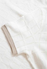 Pull en tricot blanc avec un motif en losanges texturé, doté d'un poignet côtes beige clair. Tissu doux avec des coutures détaillées.