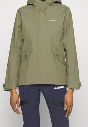 Veste à capuche verte avec poches avant boutonnées, portée avec un pantalon Adidas Terrex bleu marine.
