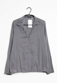 Blusa grigia con colletto, maniche lunghe e chiusura a bottoni; presenta un motivo geometrico bianco e una superficie liscia.