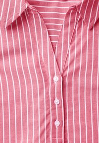 Camicia a righe rosse e bianche con colletto, chiusura frontale a bottoni e texture di tessuto liscia. Visibili diversi bottoni.