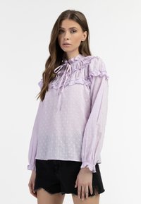 Lichtpaarse blouse met rimpelende halslijn en manchetten, voorzien van gemêleerde stippen en een gestrikte strikdetail. Draag met een zwarte shorts.