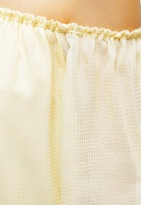 Tissu texturé jaune clair avec un motif à carreaux, doté d'une ceinture élastique. Matériau doux et transparent, design fluide, vue en gros plan.