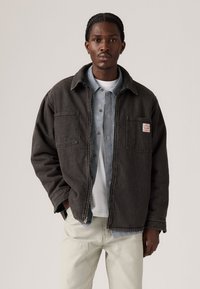 Grå denimjakke med to forlommer, iført over en blå og hvid stribet skjorte. Jakken har en afslappet pasform og struktureret stof.
