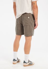 Olivengrønne fløjlsshorts med to baglommer, elastisk talje og en afslappet pasform, parret med hvide sokker og sneakers.
