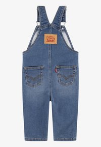 Denim overaller i mellomblått, med justerbare stropper, kobberbeslag og to frontlommer med signaturstikking.