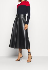 Black leather A-line skirt with a high waist, paired with a fitted navy and red long-sleeve top. Black strappy high-heeled sandals.