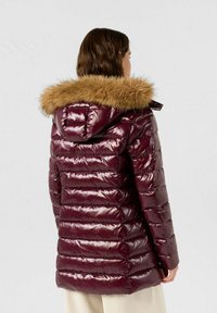 Giacca imbottita color bordeaux con finitura lucida e cappuccio bordato di pelliccia. Presenta un design trapuntato orizzontale e chiusura con zip. Tessuto caldo al tatto.