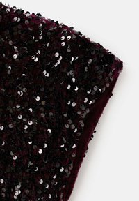 Haut bordeaux recouvert de paillettes noires, mettant en valeur une surface texturée. Le design présente une silhouette ajustée et une coupe sans manches.