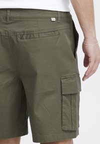 Olivenfarvede cargo shorts lavet af bomuldsblanding; har sidelommer, baglomme og et mærke med teksten "SOLID." Glat tekstur, afslappet design.