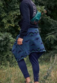 Gonna avvolgente con motivo blu e verde, con un design diagonale, tasca con zip, indossata sopra leggings blu scuro, abbinata a un hoodie nero.