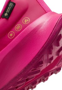 Bota de senderismo impermeable en color rosa con suela de goma texturizada. Presenta la etiqueta Gore-Tex y tres símbolos dorados que indican atributos de rendimiento.