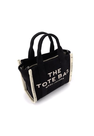 Saco de ombro retangular preto com duas alças, texto branco "THE TOTE BAG MARC JACOBS" na frente, e acabamento bege com códigos impressos.