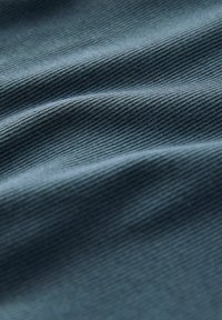 Gros plan sur un tissu bleu avec une fine texture côtière diagonale et des plis doux créant des ombres et des reflets.