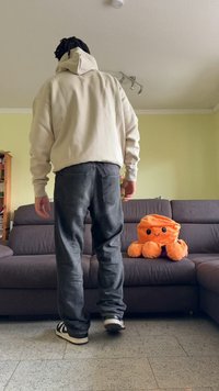 Ανοιχτό μπεζ φούτερ, γκρι τζιν, μαύρα και άσπρα αθλητικά παπούτσια. Πορτοκαλί απαλό χταπόδι σε καφέ καναπέ σε φωτεινό δωμάτιο με ανοιχτό πράσινους τοίχους.