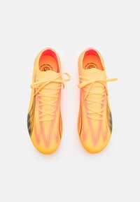 Zapatillas deportivas de un brillante color amarillo con un diseño degradado en rosa, parte superior texturizada, acentos negros y cordones planos. Diseñadas para uso deportivo o recreativo.