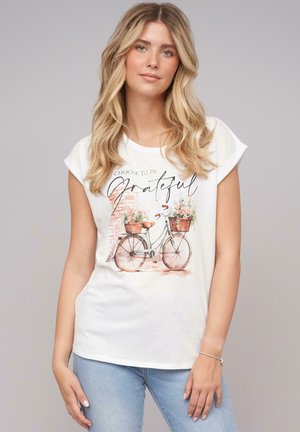 White t-shirt with short sleeves featuring a bicycle illustration. The bike has baskets with flowers. Text reads "Choose to be Grateful."